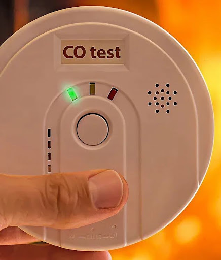 Hand testing a carbon monoxide alarm's CO test button, part of home heating safety checks in Melbourne.